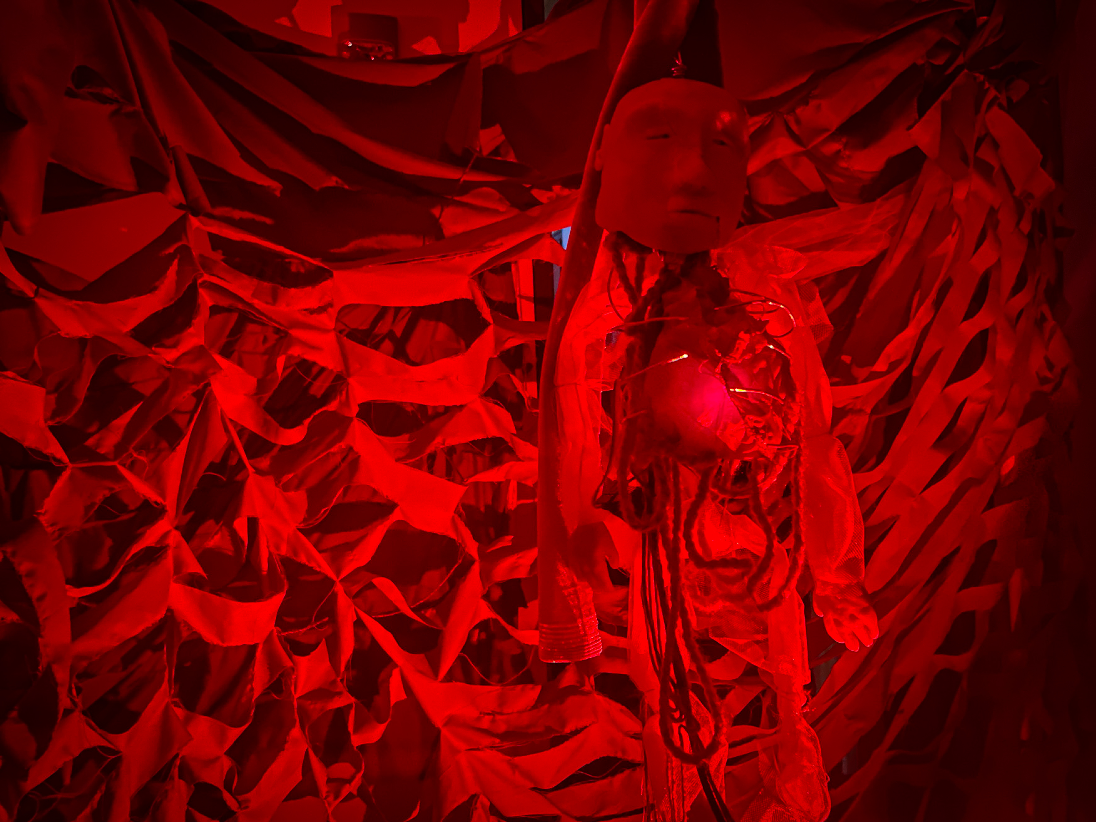 A doll with an exposed heart in a red-lit room designed to look like a blood vessel