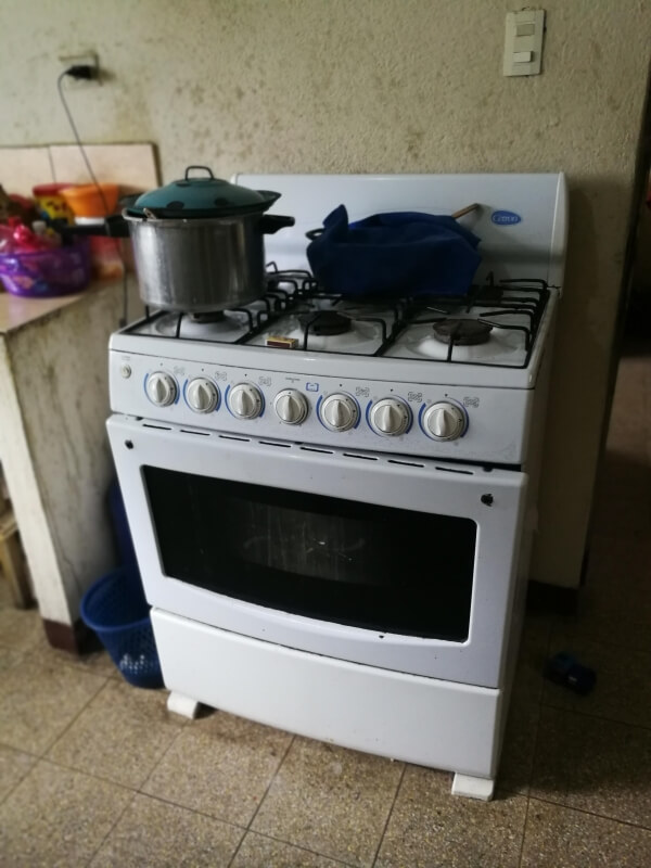 A white gas range with several pieces of cookware on the stovetop is located on a beige tile floor against a beige wall. Several food items are on the countertop to the left.