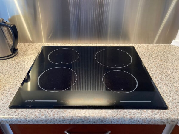 An black electric stovetop on an off-white speckled countertop. There is a water kettle in the top left corner. 