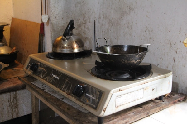 A diagonal view of a stovetop burner on a counter. A metal kettle is on one burner and a darker metal pan is on the other.