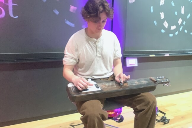 A male Harvard student playing a homemade lap steel guitar