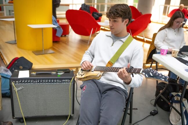 A Harvard student sitting and playing an electric guitar