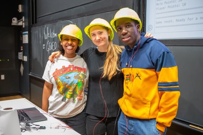 Three Harvard students wearing yellow construction hats