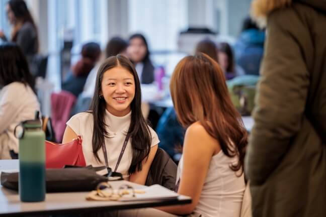 Two female students sitting at a table interacting