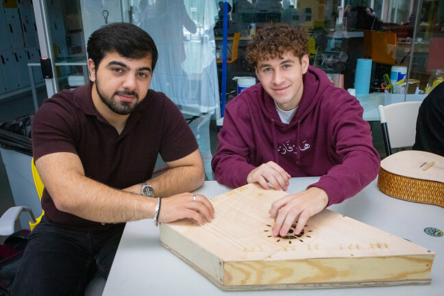 Harvard students Saleh Yassin and Aram Bagdasarian next to a wooden stringed instrument called a kanun