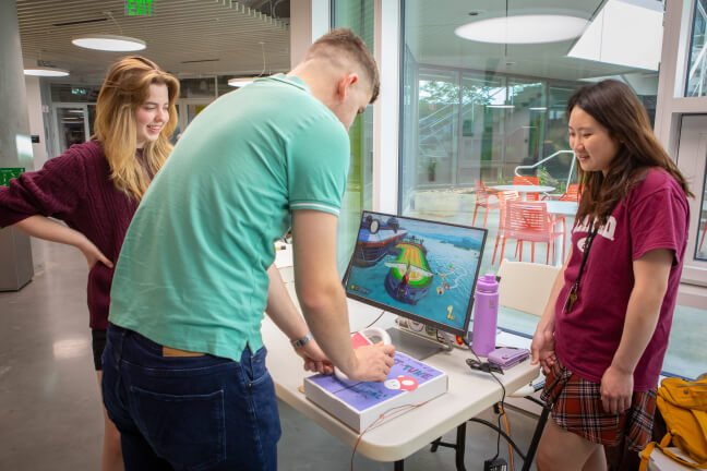 Harvard students Cassidy Crabb and Grace Hur showing someone how to use their steering wheel musical instrument