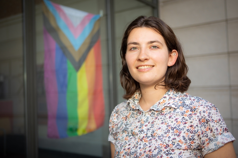 Ashley Cavanagh in front of Pride Flag at Maxwell Dworkin