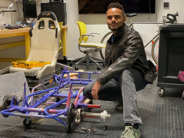 Adam Reid kneels by the frame of his club's electric go-kart project