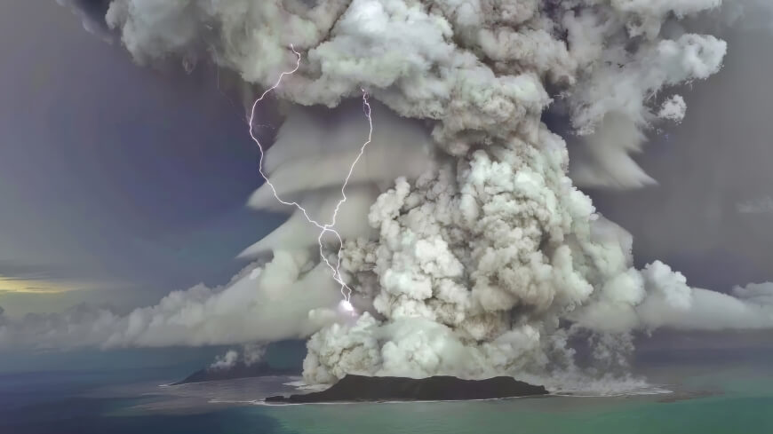 Volcano erupting with lightning in the plume on an island surrounded by ocean