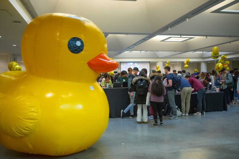 A large balloon shaped like a yellow rubber duck next to a crowd of students at a Harvard computer science festival in Cambridge