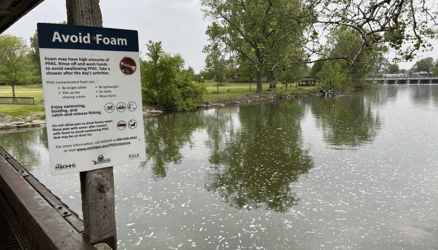 A white sign along a river with trees and grass in the background