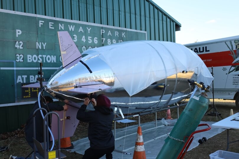 A large silver-colored blimp being filled with helium by Harvard SEAS students at Crow Island Airpark in Stow, Mass.