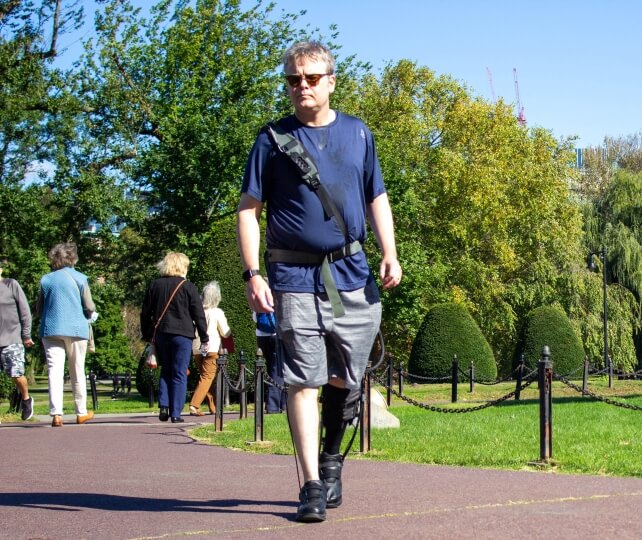 A man walking through a park wearing a robotic exosuit on his left leg