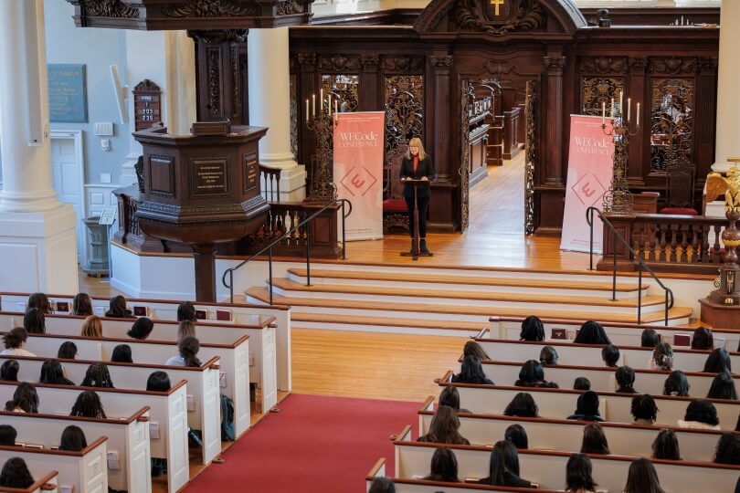 Esther Wojcicki at a lectern in front of a group of female students in a church