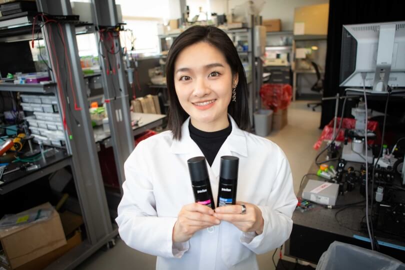 Harvard SEAS student Xinge Diana Zhang wearing a white lab coat and holding up two bottles of skincare products