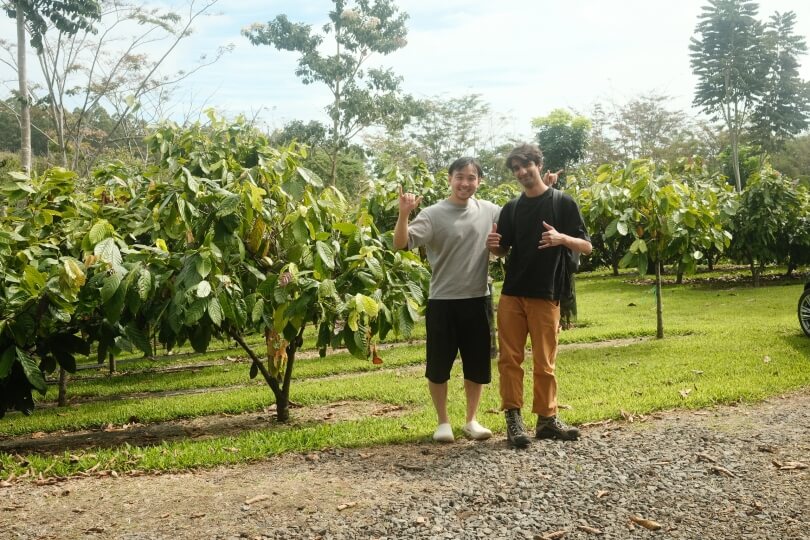 Harvard SEAS GSD students Darren Chin and Akhil Dayal in front of small trees on a farm in Hawaii