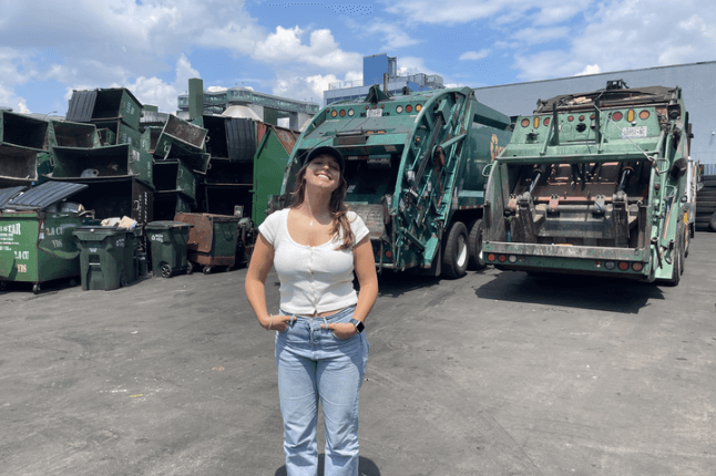 SEAS junior Sofia Giannuzzi standing in a parking lot front of a fleet of garbage trucks