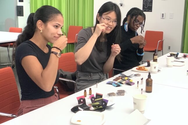 Three Harvard students smelling perfume samples and ingredients, sitting next to a white table