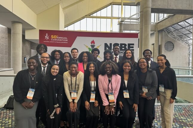 A large group of Harvard students in front of a sign for the National Society of Black Engineers national convention