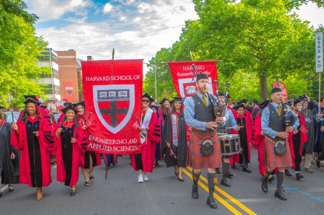 Harvard SEAS and GSAS banners, bagpipers, students in Crimson regalia