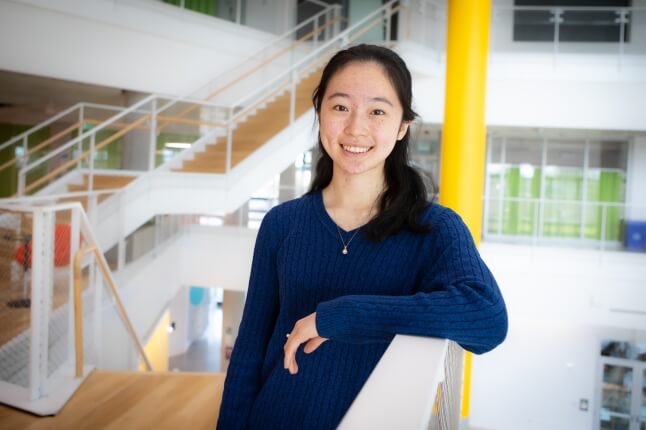 Harvard SEAS student Lauren Chen wearing a blue shirt in front of a staircase and yellow pole at the Scienc and Engineering Complex in Allston