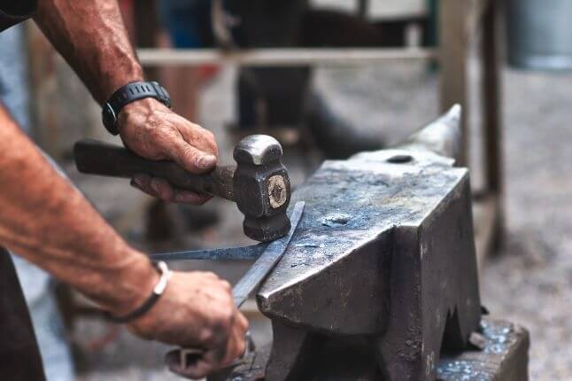 A person hammering a metal rod on an anvil, engaged in blacksmithing work