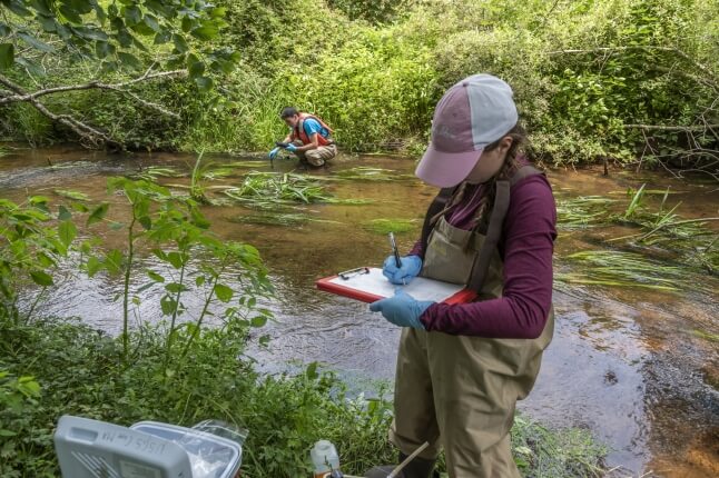 image of women standing in a river taking notes 