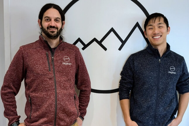 Harvard SEAS alumni Benjamin “Zags” Zagorsky and Kevin Fan in front of the logo for software company, Zagaran, Inc.