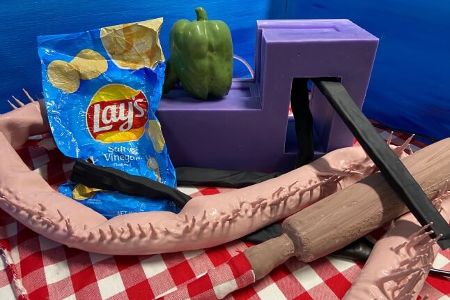 chip bag, bell pepper, rolling pin, and abstract objects on a checkered tablecloth