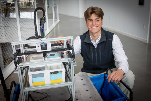 Harvard SEAS student Michael Kuhl kneeling next to a robot