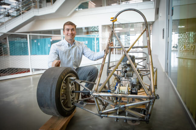 Harvard SEAS student Jack Anderson kneeling next to an unfinished Formula SAE racecar