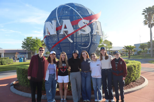 Harvard SEAS students in front of a blue NASA logo statue at Kennedy Space Center in Florida