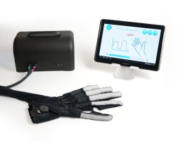 A glove attached to a small black box and small screen rests on a white desktop.