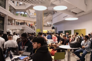 A large crowd of students sitting at tables and standing on stairwells at HackHarvard 2023