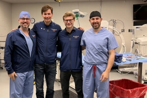 Two men wearing hospital scrubs, two wearing blue jackets with the logo for the company EndoShunt, in front of medical equipment