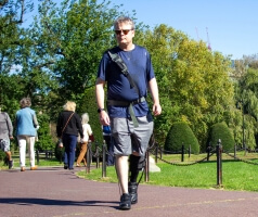 A man wearing a robotic exosuit and walking through a park