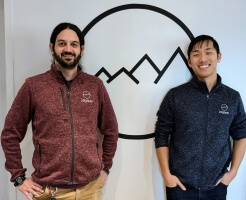 Harvard SEAS alumni Benjamin “Zags” Zagorsky and Kevin Fan in front of the logo for software company, Zagaran, Inc.