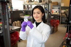 Harvard SEAS student Xinge Diana Zhang wearing a white lab coat and holding up an enzyme slide