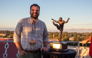harvard SEAS alum Michael Mancinelli, S.B. '15, MS/MBA '21, next to a football trophy