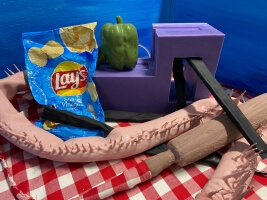 chip bag, bell pepper, rolling pin, and abstract objects on a checkered tablecloth