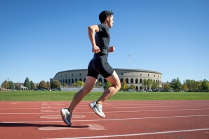 man runs on track with stadium in background