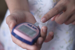Close-up of a person’s hands holding a blood glucose meter while using a finger to prepare for a blood sugar test.