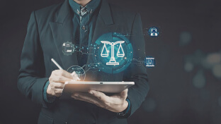 Alt text:  Person in a dark suit holding a digital tablet with a stylus, overlaid with glowing blue icons representing law and technology, including a central scale of justice, a gavel, and abstract AI and data symbols, suggesting the intersection of artificial intelligence and legal decision‑making